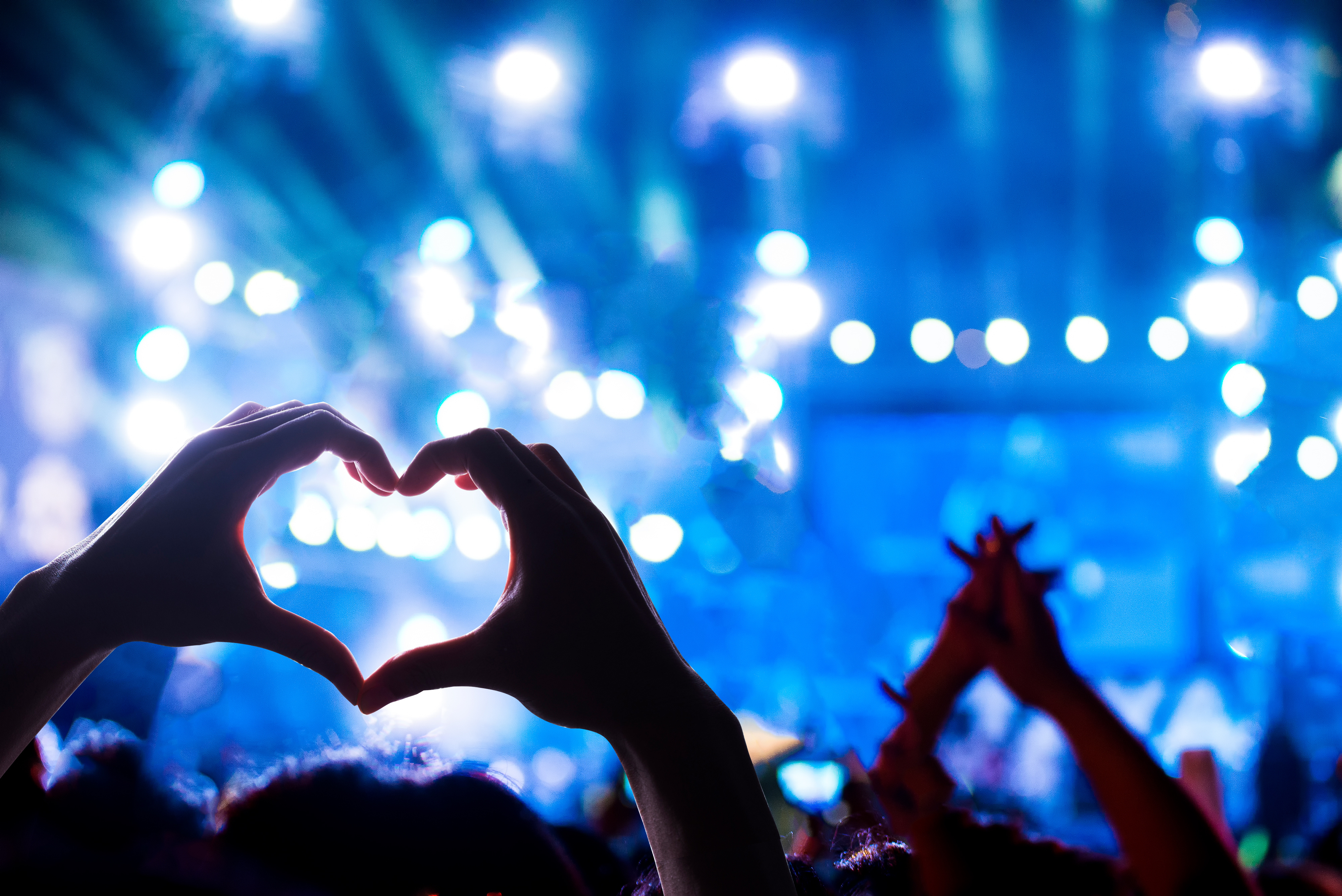 Crowd of Audience at during a concert with silhouette of a heart shaped hands shadow, light illuminated is power of music concert