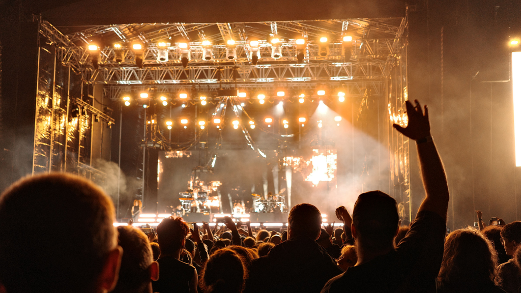 Beyond the Announcement: What Actually Drives Successful Live Event Marketing? 2 Concertgoers cheering with raised hands as a live band performs on a brightly lit stage.
